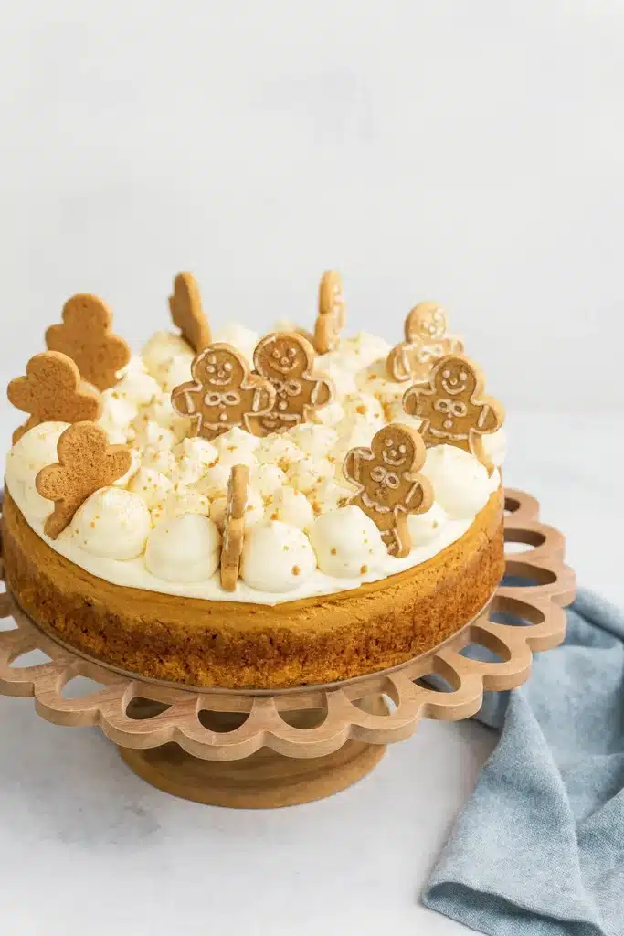 Gingerbread Cheesecake Recipe | Creamy, Festive & Delicious 5 Gingerbread cheesecake topped with cream frosting and mini cookies on white-gray table