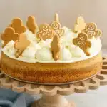 Gingerbread cheesecake topped with cream frosting and mini gingerbread cookies on a wooden stand