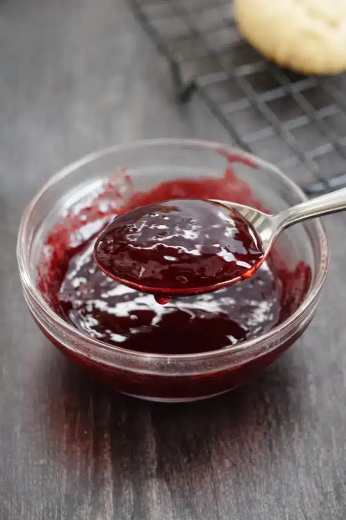 Raspberry Thumbprint Cookies with Icing – Simple Joy 10 Spoon lifting glossy raspberry jam from a glass bowl