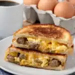 Golden breakfast grilled cheese sandwich with eggs and sausage on white plate