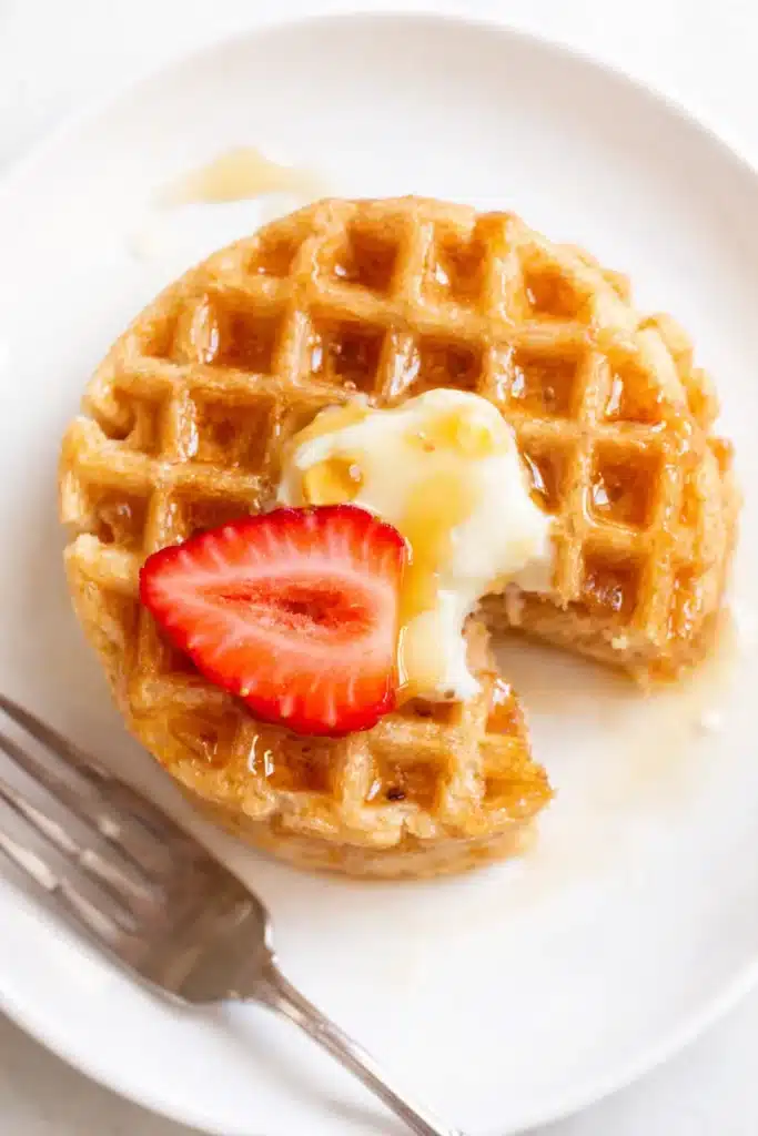 Single protein waffle with butter, syrup, and strawberry slice on a white plate