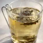 Glass mug of freshly brewed green tea with floating leaves and red buds