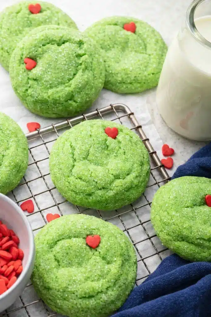 Grinch sugar cookies cooling on a wire rack with red heart sprinkles