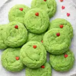 Grinch sugar cookies with red hearts on white plate, festive Christmas dessert