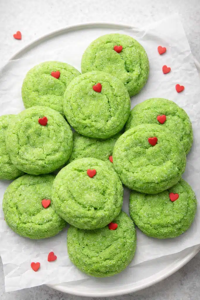 Grinch sugar cookies with red hearts on white plate, festive Christmas dessert