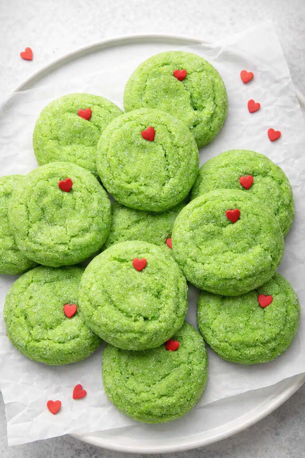 Grinch sugar cookies with red hearts on white plate, festive Christmas dessert