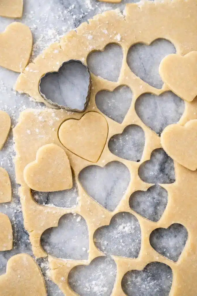 Heart-shaped cookie dough with metal cutter on floured surface