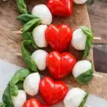 Heart-shaped tomato Caprese skewers with mozzarella and basil on a wooden board