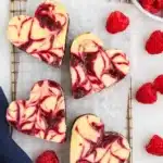 Heart shaped raspberry cheesecake brownies on parchment with fresh raspberries