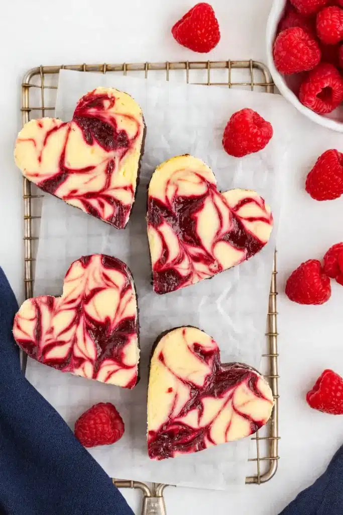 Heart shaped raspberry cheesecake brownies on parchment with fresh raspberries