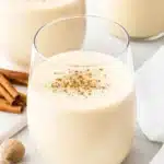 Homemade eggnog in cups topped with nutmeg and cinnamon on a wooden table