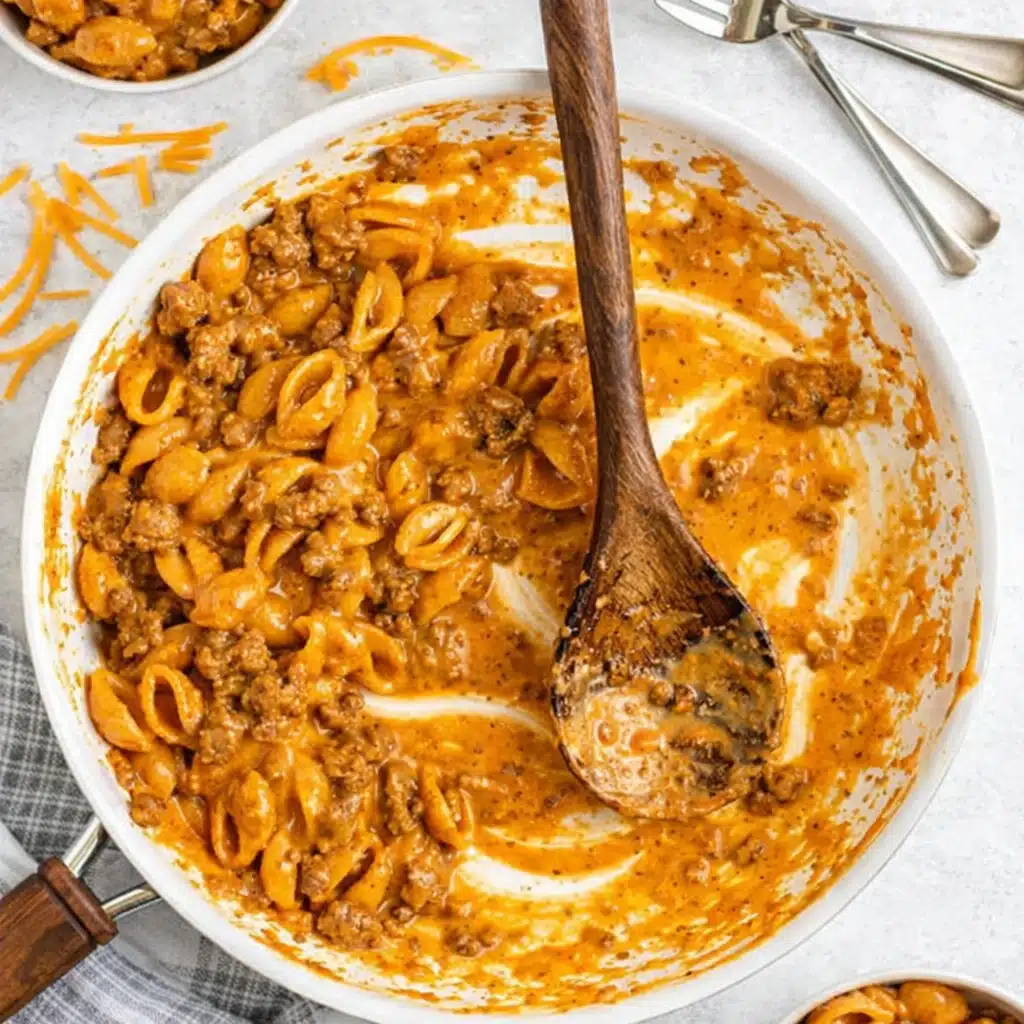Homemade hamburger helper in skillet with wooden spoon and cheese sauce
