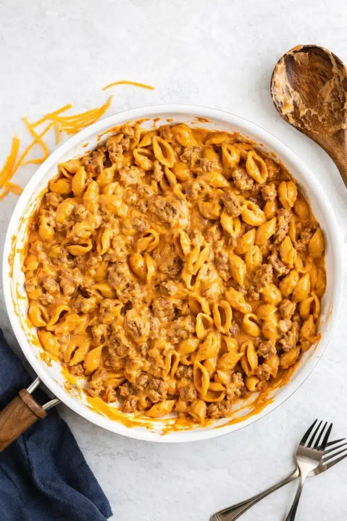 Homemade hamburger helper in white skillet with cheese sauce and blue napkin