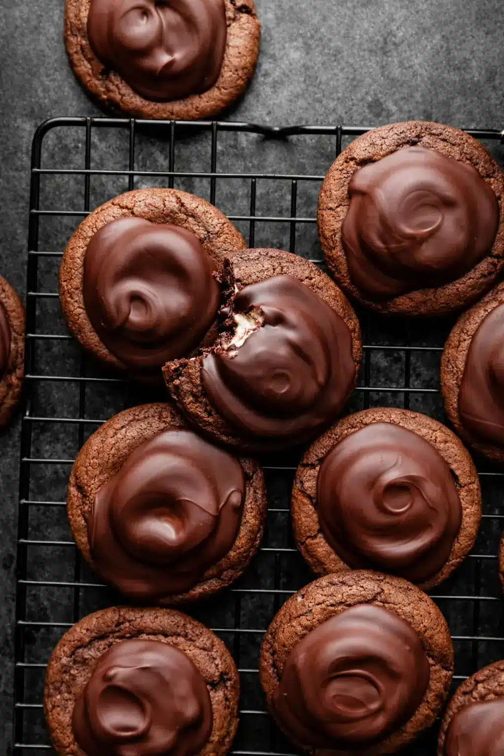 Hot cocoa cookies with glossy chocolate topping and marshmallow center on a cooling rack