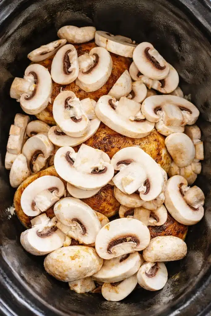 Mushrooms layered over seared chicken in a crock pot for creamy chicken marsala