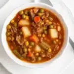 Old-fashioned vegetable beef soup with potatoes, peas, and carrots in a rustic white bowl