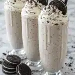 Cookies and cream milkshake topped with whipped cream and Oreo cookies on a marble surface