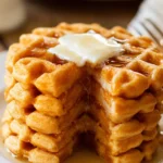 Stack of golden protein waffles with melting butter and syrup on a white plate