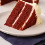 Red velvet cake slice with cream cheese frosting on white plate