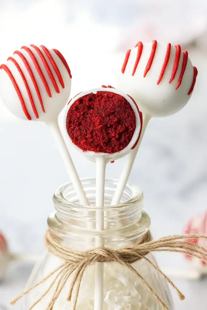 Red Velvet Cake Pops – Easy, Sweet & Irresistible Treats 7 Red velvet cake pops with red drizzle in glass jar on brown wooden table