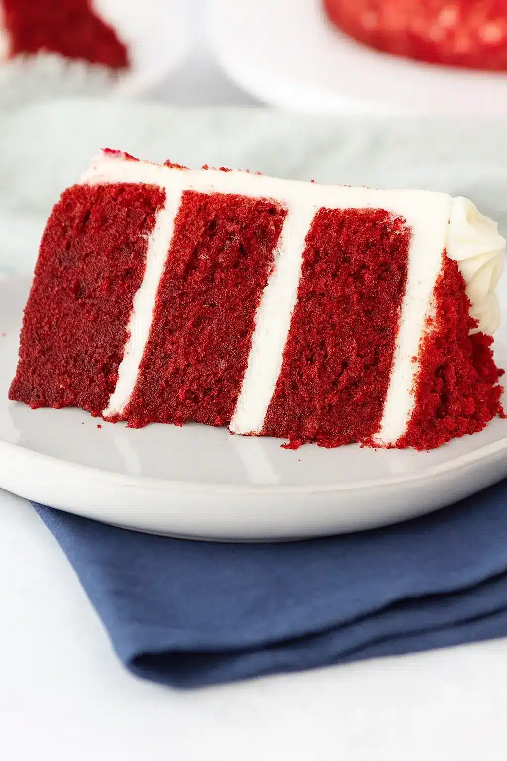 Slice of red velvet cake with cream cheese frosting on white plate