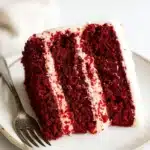 Slice of red velvet cake with cream cheese frosting on a plate