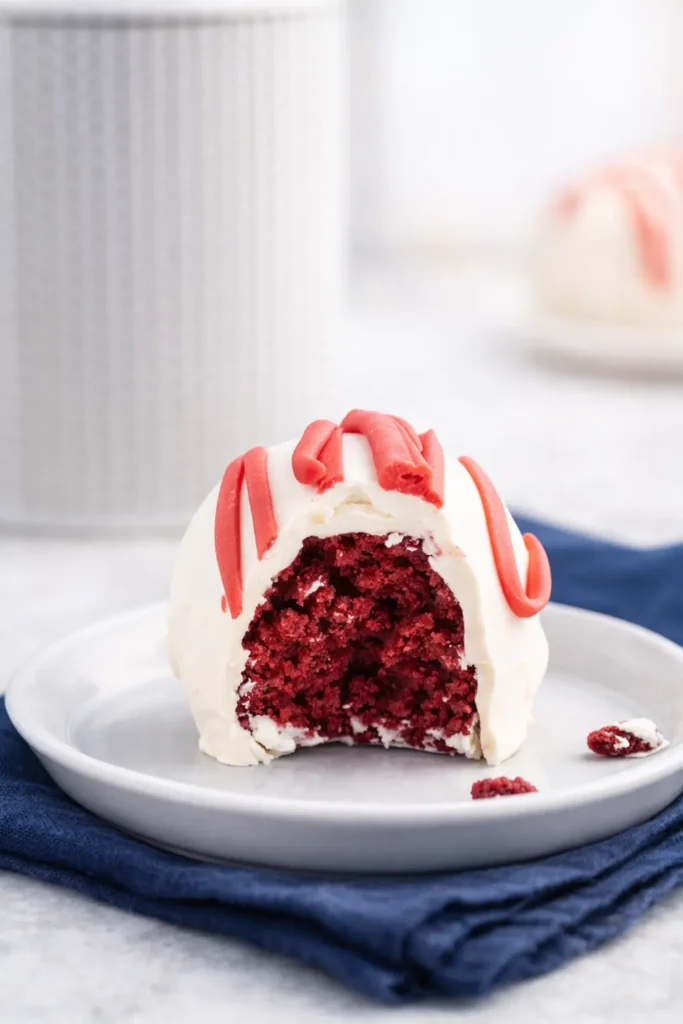 Bitten red velvet cheesecake bite on white plate with red drizzle and blue napkin