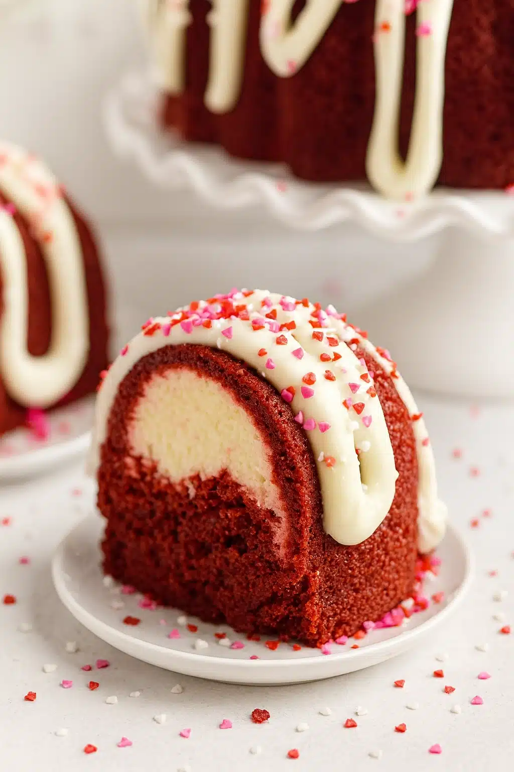 Red velvet cream cheese bundt cake slice with icing and heart sprinkles