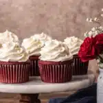 Red velvet cupcakes with cream cheese frosting on a cake stand beside red roses