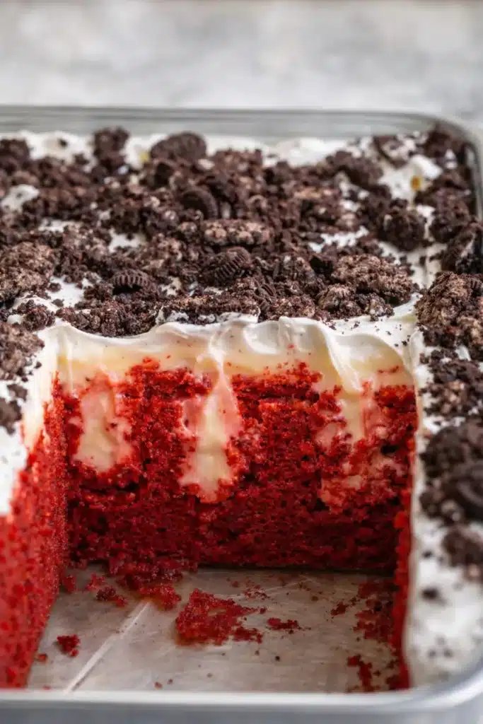 Red velvet poke cake in baking pan with cheesecake pudding and Oreo topping