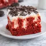 Red velvet poke cake slice with whipped topping and crushed cookies
