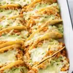 Crispy rotisserie chicken tacos with melted cheese and lettuce in a baking dish