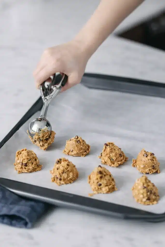 No Bake Protein Balls – Simple and Powerful Snack 14 Scooping no bake protein ball dough onto tray with oats and chocolate chips