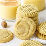 Soft eggnog cookies with icing drizzle and glasses of eggnog in cozy holiday lighting