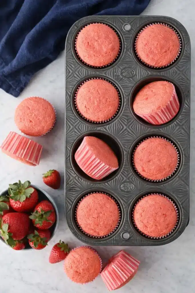 Freshly baked strawberry cupcakes in muffin pan with blue napkin and strawberries