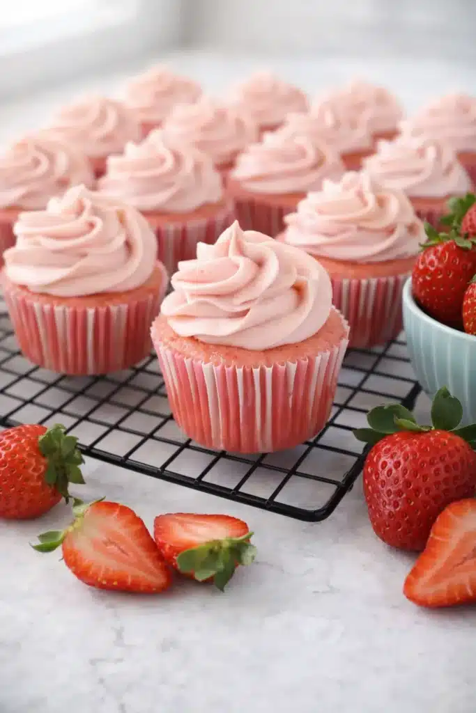 Strawberry cupcakes with pink frosting on cooling rack and fresh strawberries