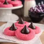 Pink strawberry kiss cookies topped with chocolate truffles on a wooden board
