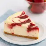 Slice of strawberry swirl cheesecake on white plate with fresh strawberries