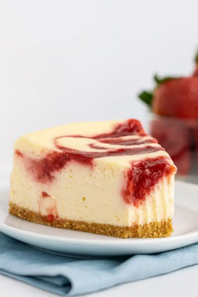 Strawberry Swirl Cheesecake | Romantic & Delicious Dessert 9 Slice of strawberry swirl cheesecake on white plate with fresh strawberries in background