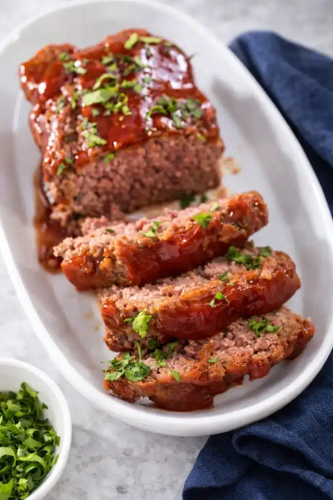 Juicy sliced meatloaf with ketchup glaze and parsley in white dish