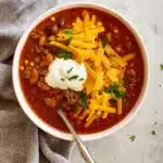 Hearty taco soup topped with cheese, sour cream, and tortilla strips in a white bowl