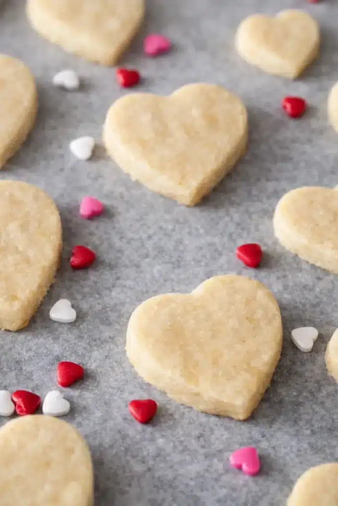 Unbaked heart-shaped Valentine cookies on parchment with candy hearts