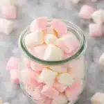 Glass jar filled with pastel pink and white butter mints on light stone surface