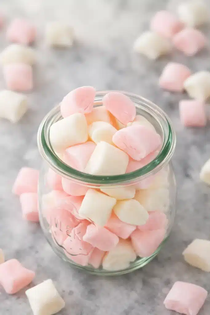 Glass jar filled with pastel pink and white butter mints on light stone surface