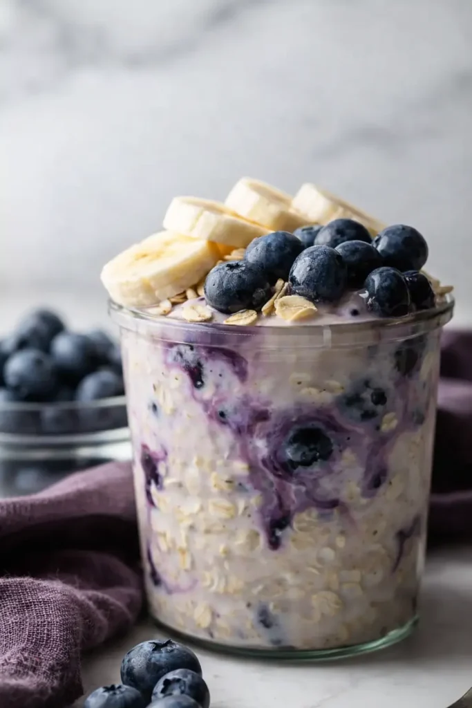 Blueberry banana overnight oats in a glass jar topped with fruit