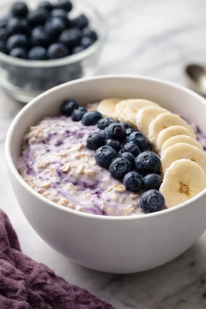 Blueberry banana overnight oats in a white bowl on marble surface