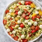 Creamy Caprese pasta salad with mozzarella, cherry tomatoes, and basil in a white bowl