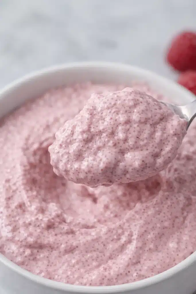  Spoon lifting creamy raspberry chia seed pudding from a white bowl