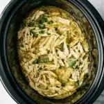 Shredded crockpot salsa verde chicken garnished with cilantro in a slow cooker