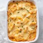 Golden butternut squash casserole topped with cheese and thyme in white baking dish